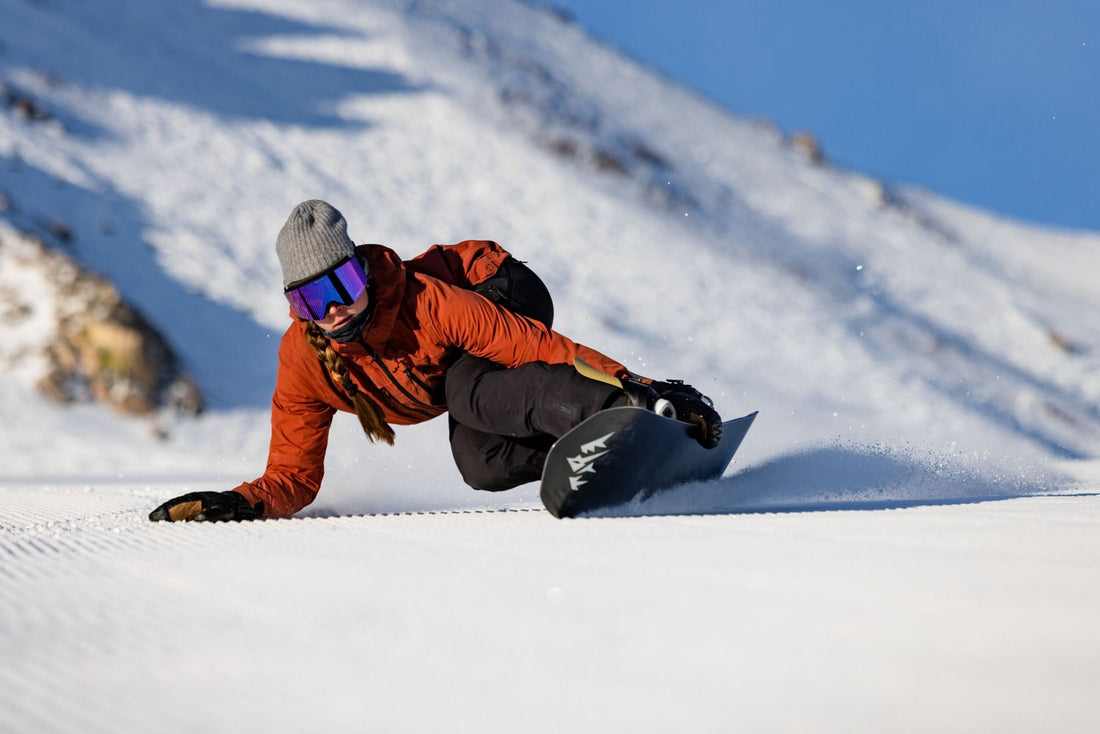 A female snowboarder with a long hair braid carves a turn on a fresh piste.
