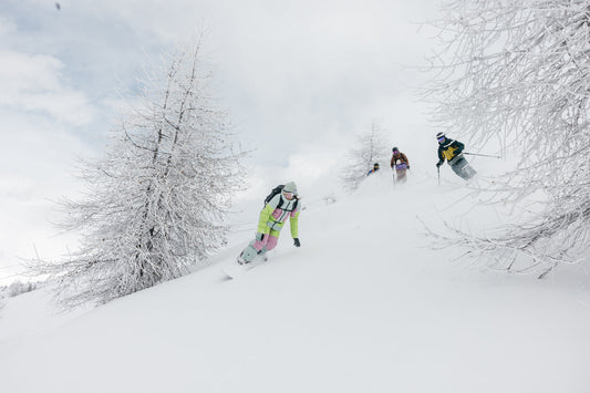 A snowboarder in a bright green rental outfit rides through deep snow with three skiers.