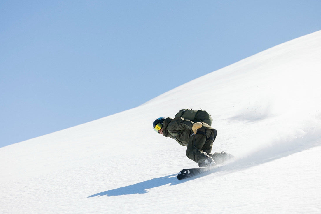 A snowboarder wearing Bergtagen snowboard outerwear leans into a turn in deep powder snow.