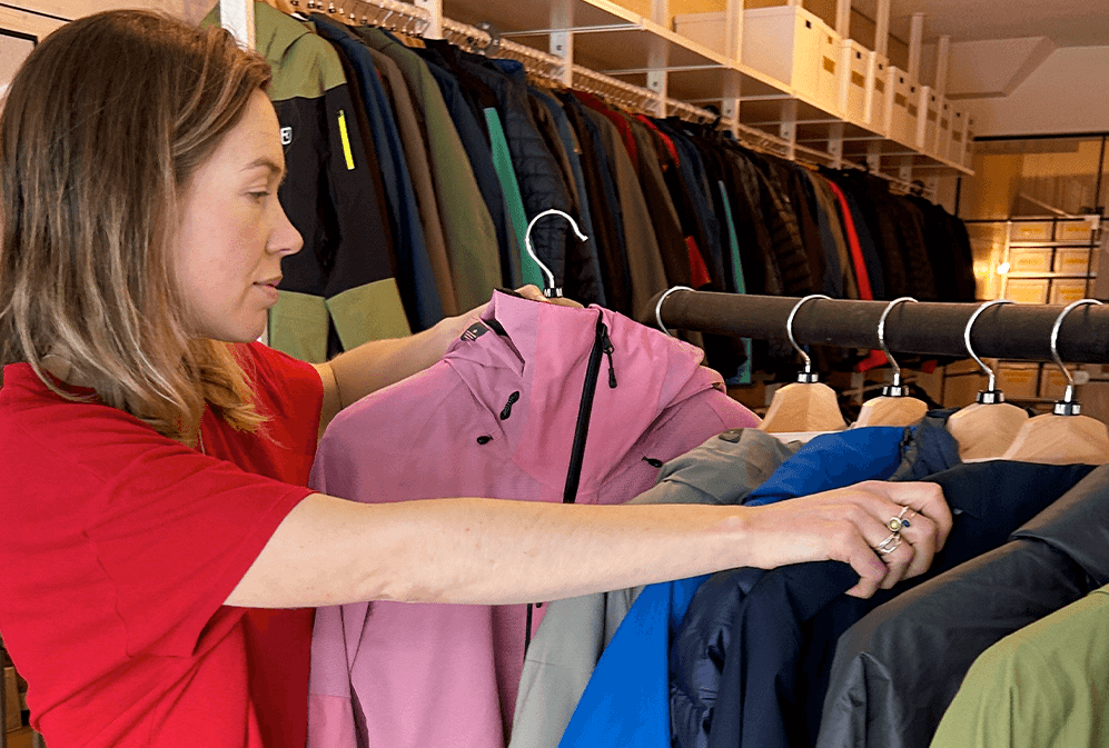 A woman in a red t-shirt looks through rack of colourful jackets while holding a pink jacket.