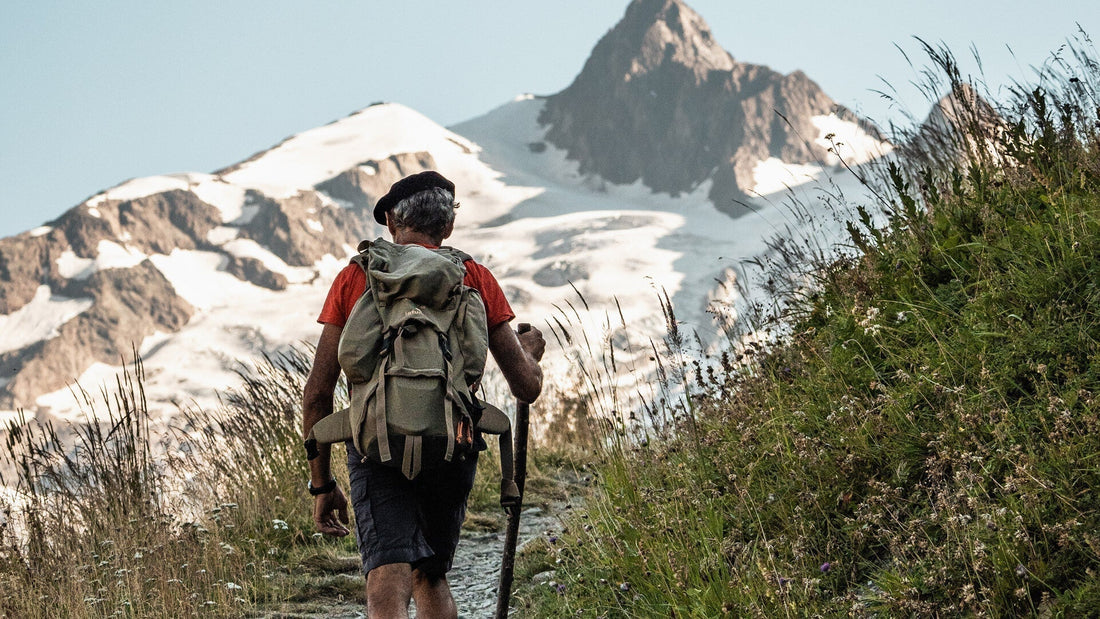 An older gentleman in a red shirt with a backpack hikes in the mountainous area of Les Champieux