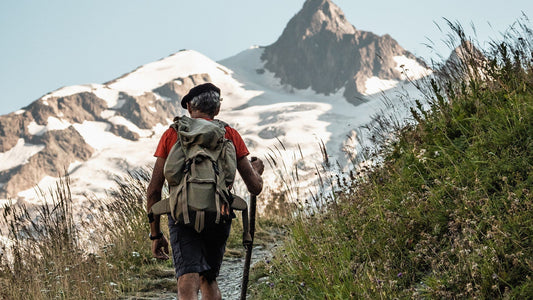An older gentleman in a red shirt with a backpack hikes in the mountainous area of Les Champieux