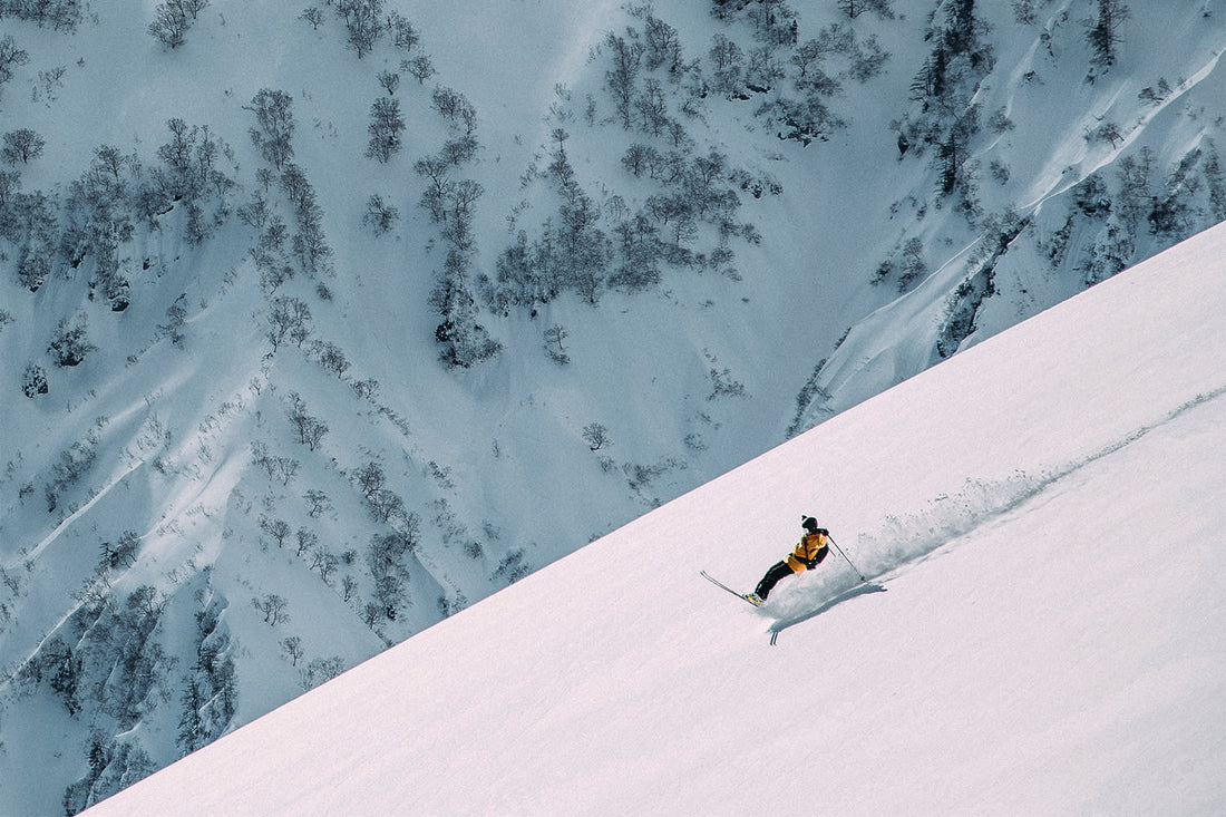 A skier straight lines a powder field and leans right back so he is riding on the tail of his skis.