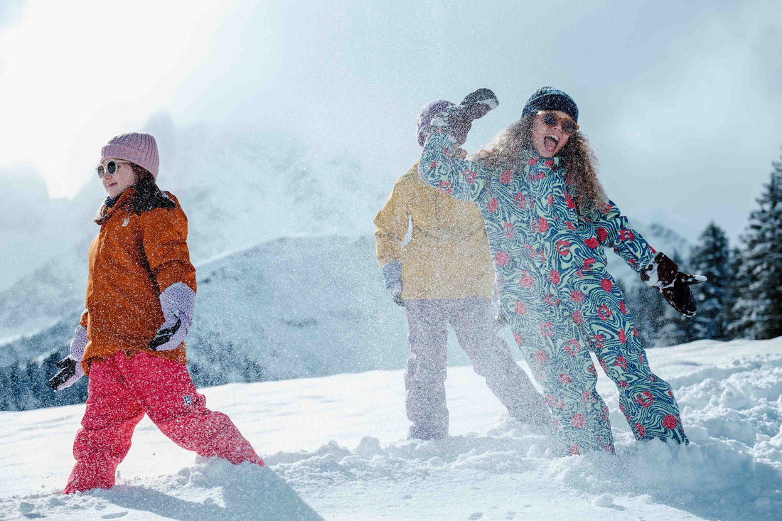 Three children dressed in colourful winter clothing kick up snow as they play in the mountains