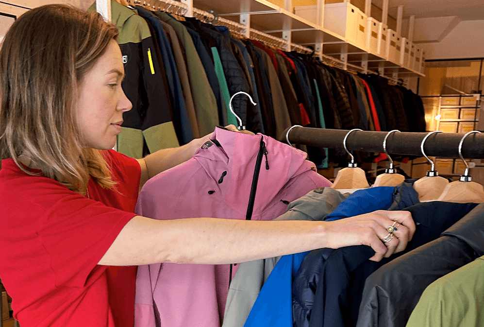 A woman in a red t-shirt looks through rack of colourful jackets while holding a pink jacket. 