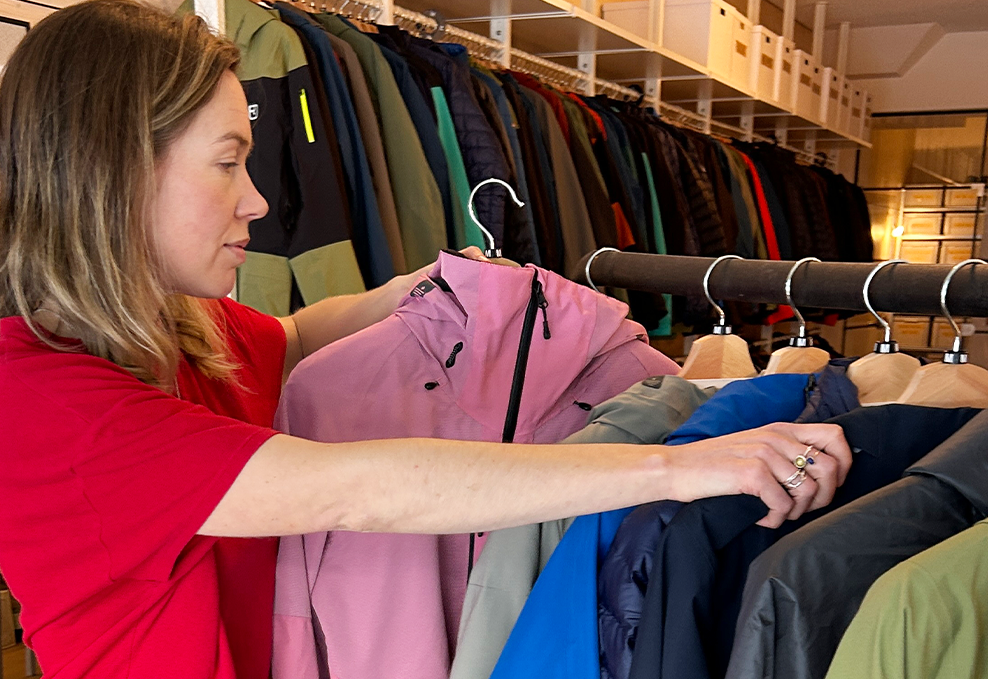 A woman in a red t-shirt looks through rack of colourful jackets while holding a pink jacket. 