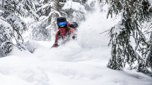 Woman in a red ski jacket skiing waist deep powder in a forest in Davos.